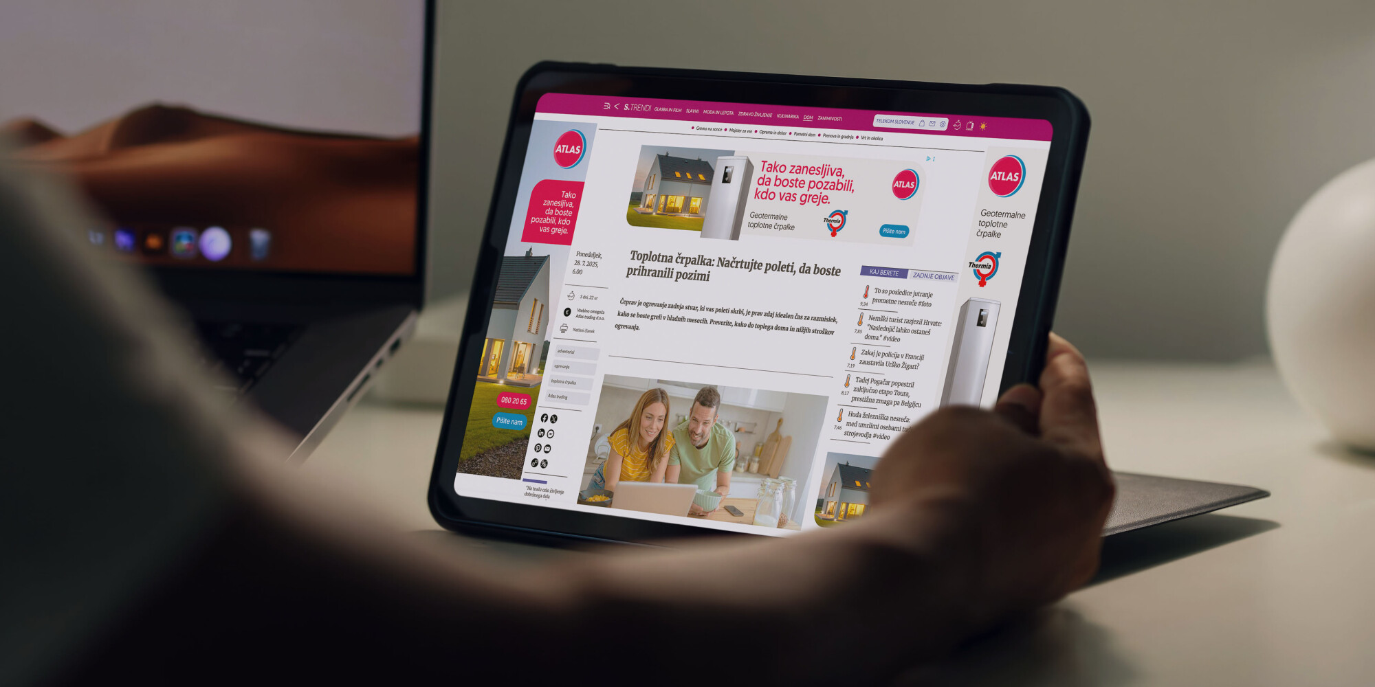 Roka, ki drži tablični računalnik, na katerem je spletni oglas za toplotne črpalke Atlas.