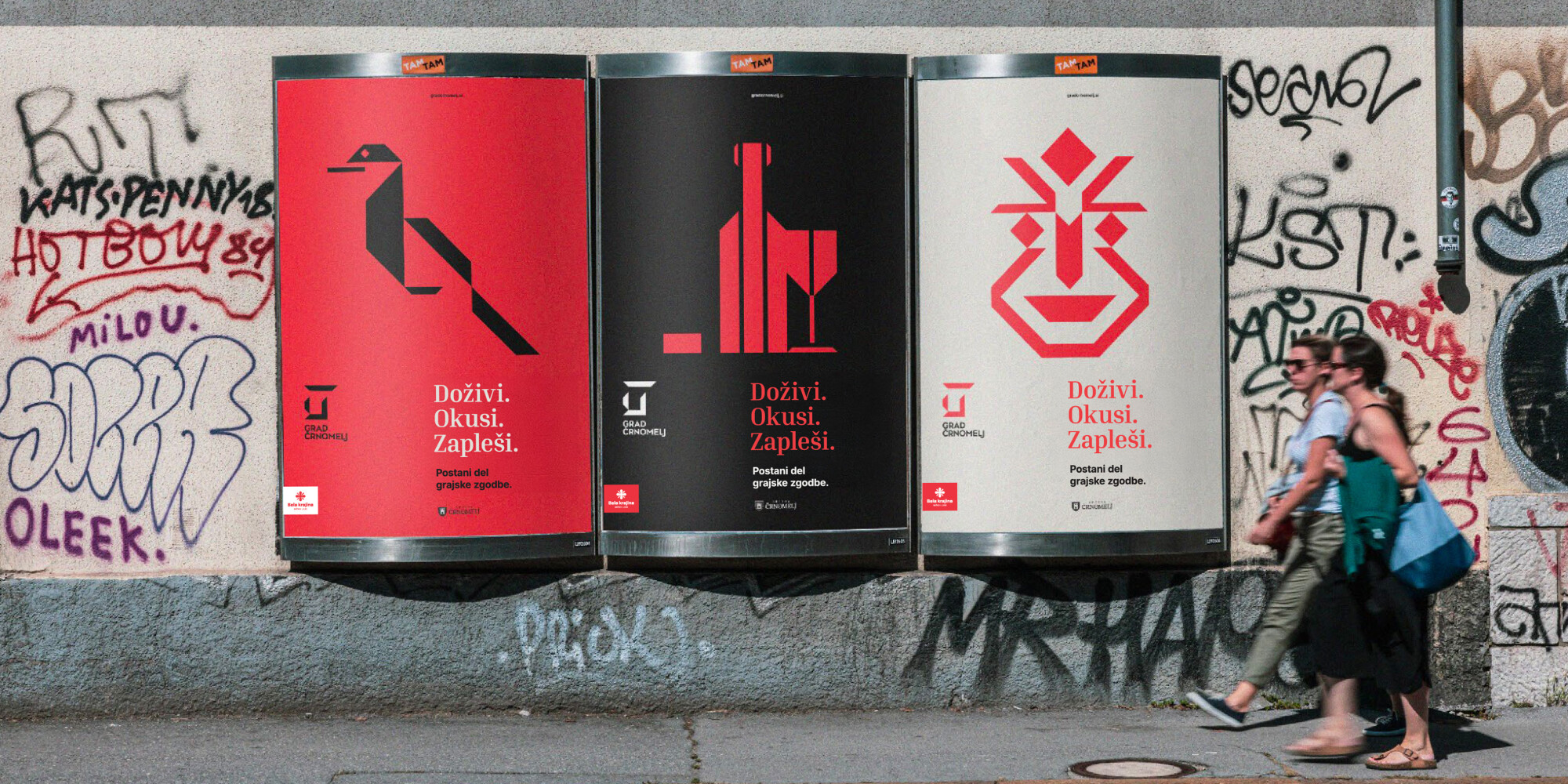 Three posters on a city street. The first poster has a red background and features a black stylised bird motif; the second poster has a black background with a red stylised bottle and glass motif; the third poster has a grey background with a red face mot