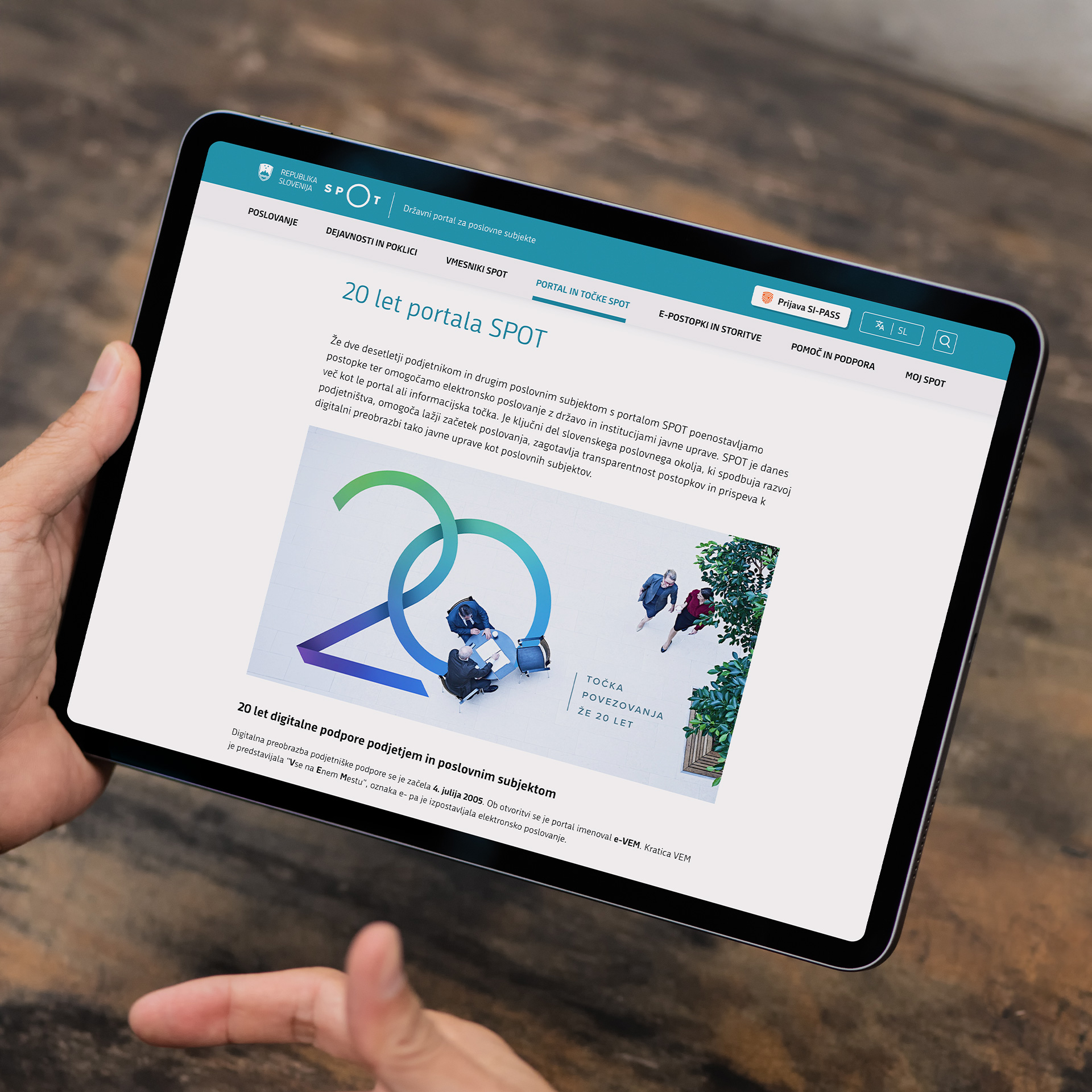 Moške roke držijo tablični računalnik. Na zaslonu je vstopna stran 20 let portala SPOT